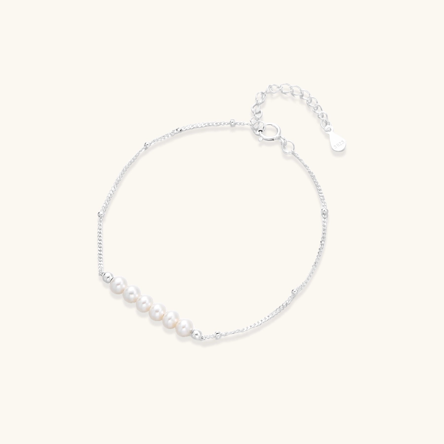 Dainty sterling silver bracelet with small white baroque pearls and adjustable chain on neutral background.