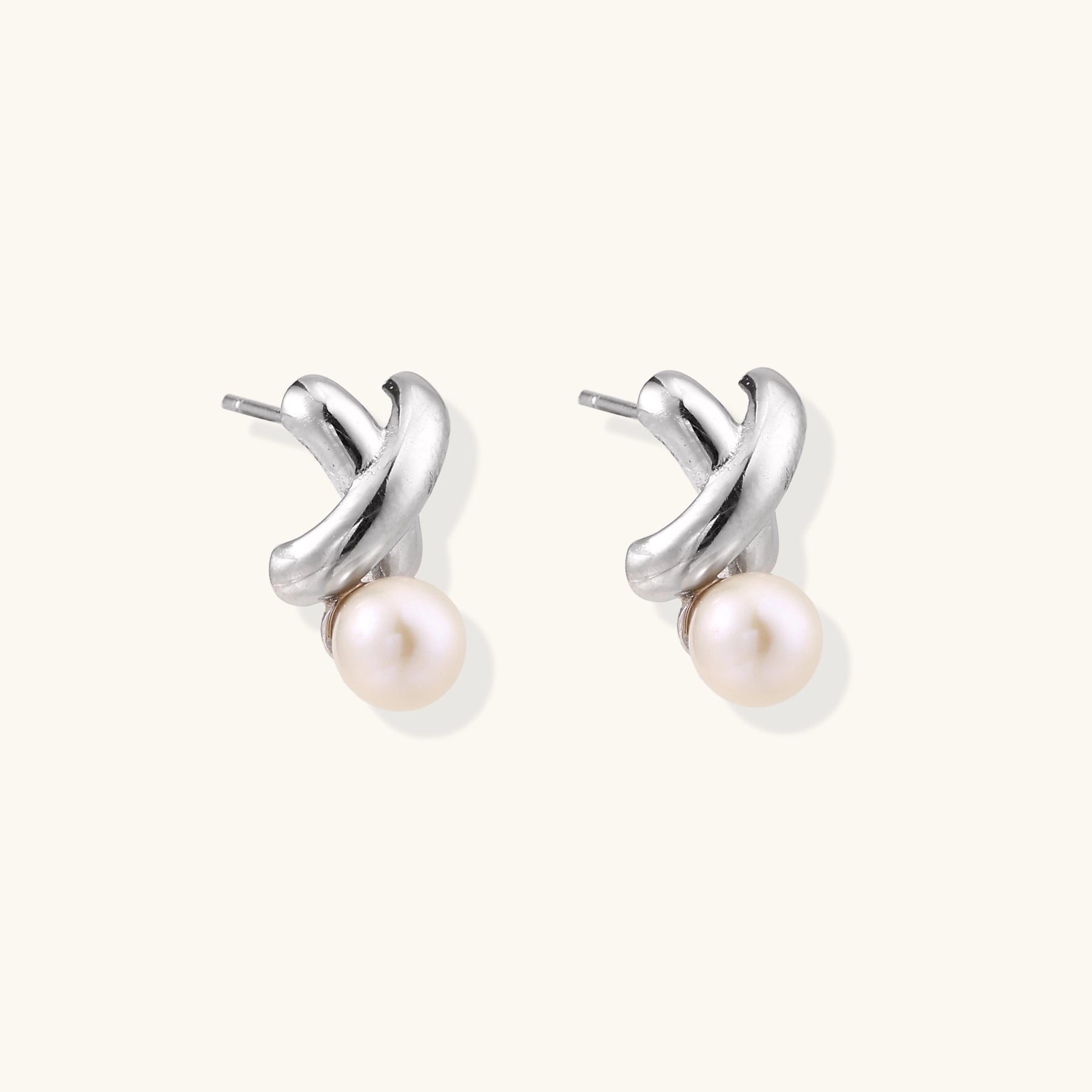 Sterling silver twisted stud earrings with round freshwater pearls on cream background, showing polished finish