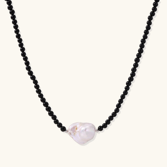Elegant necklace with black agate beads and iridescent baroque freshwater pearl centerpiece on white background.