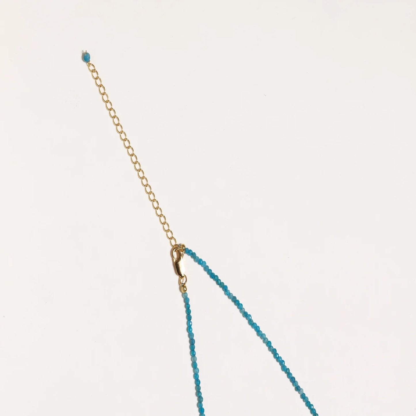 Delicate gold vermeil necklace with teal apatite beads and freshwater pearl on white background.