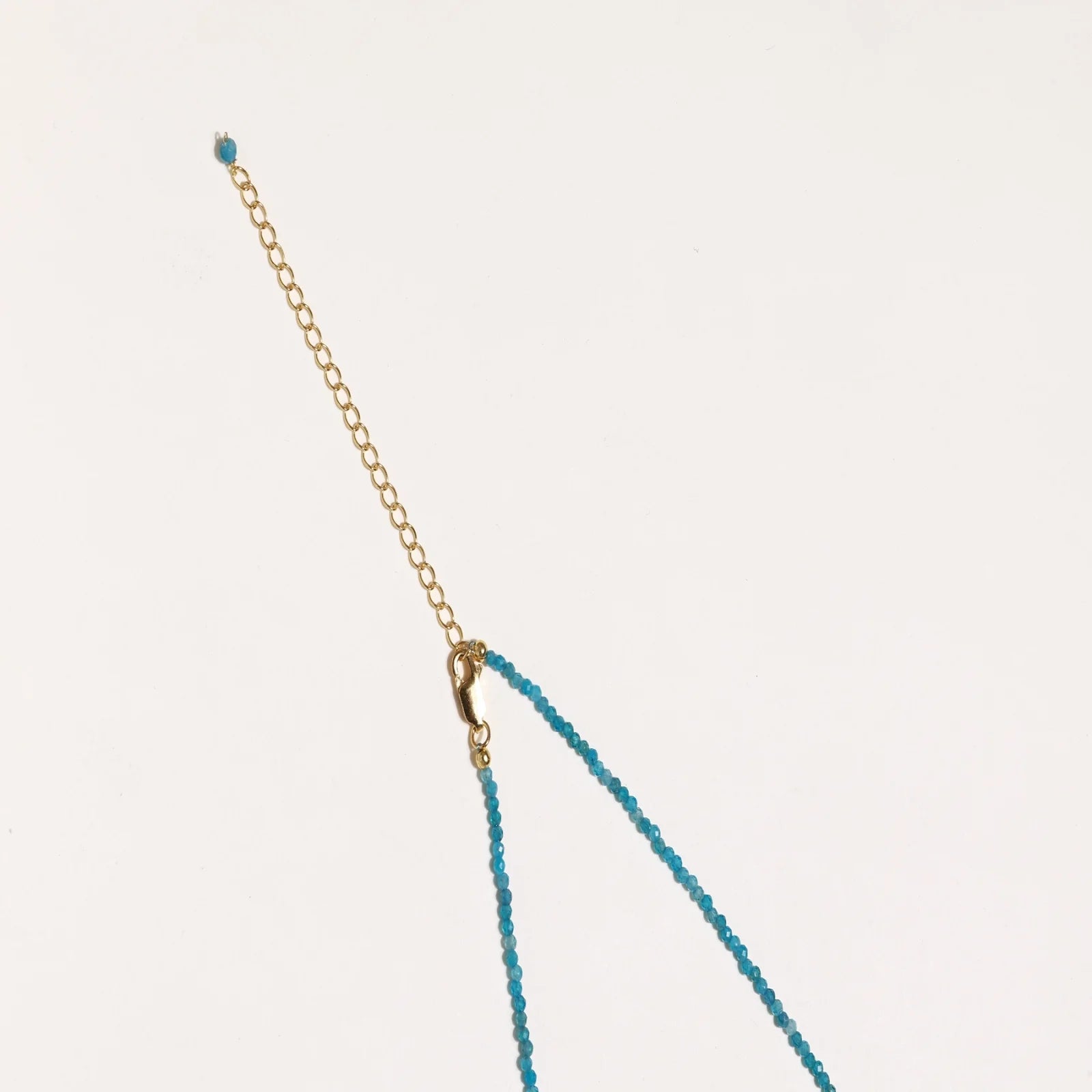 Delicate gold vermeil necklace with teal apatite beads and freshwater pearl on white background.