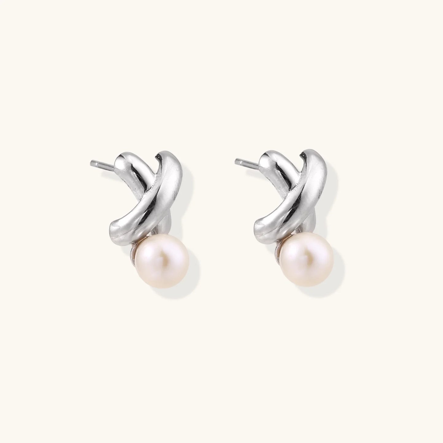 Rhodium-plated silver earrings with twisted X design and freshwater pearl drops on beige background