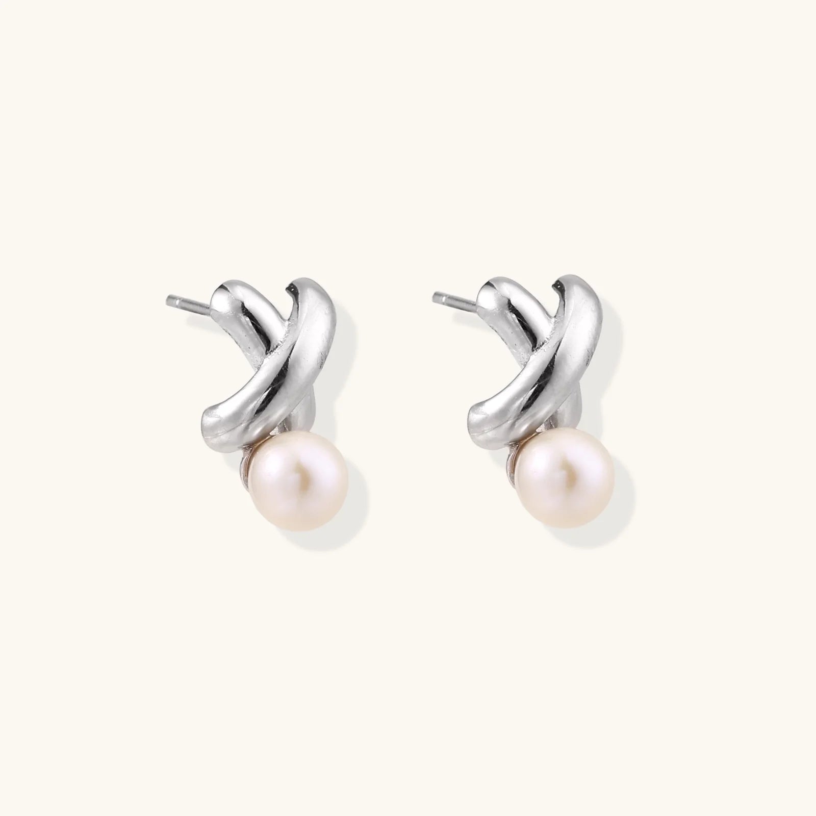Rhodium-plated silver earrings with twisted X design and freshwater pearl drops on beige background