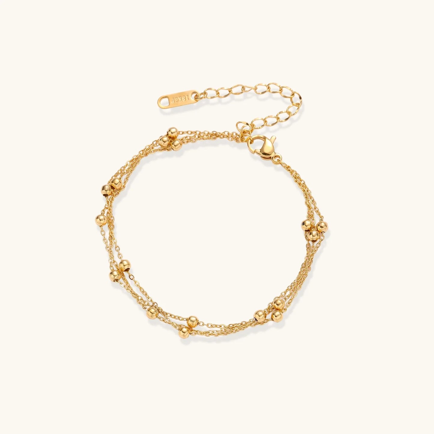 Three-strand gold-plated bracelet with clustered ball beads and adjustable clasp on cream background