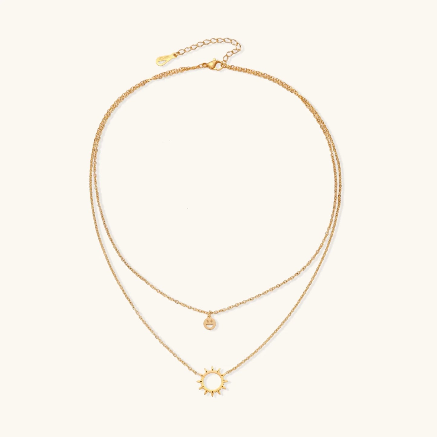 Gold layered necklace set with sunburst and smiley face pendants on delicate chains against white background.