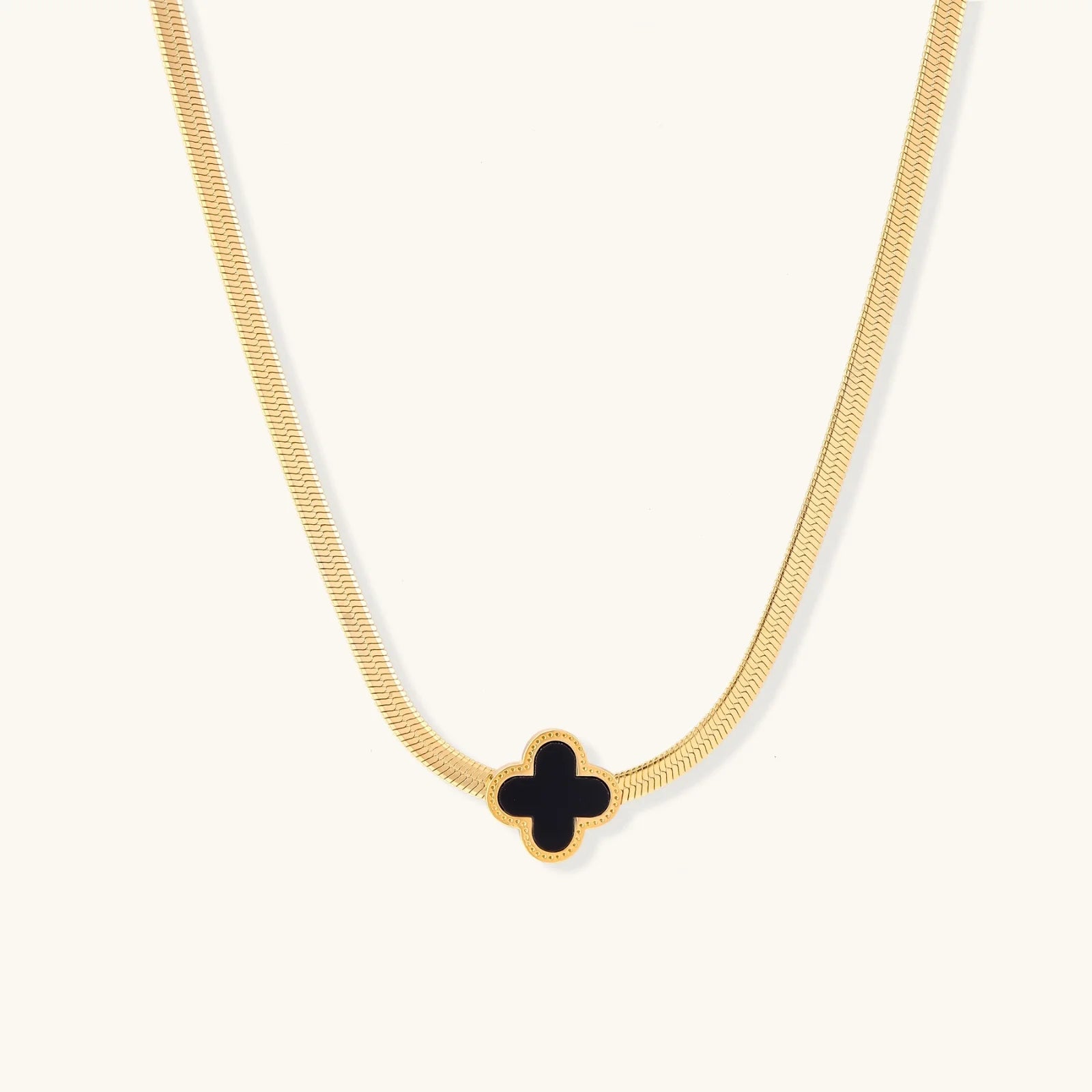 Dainty 18K gold-plated herringbone chain necklace with black enamel quatrefoil clover pendant on white background