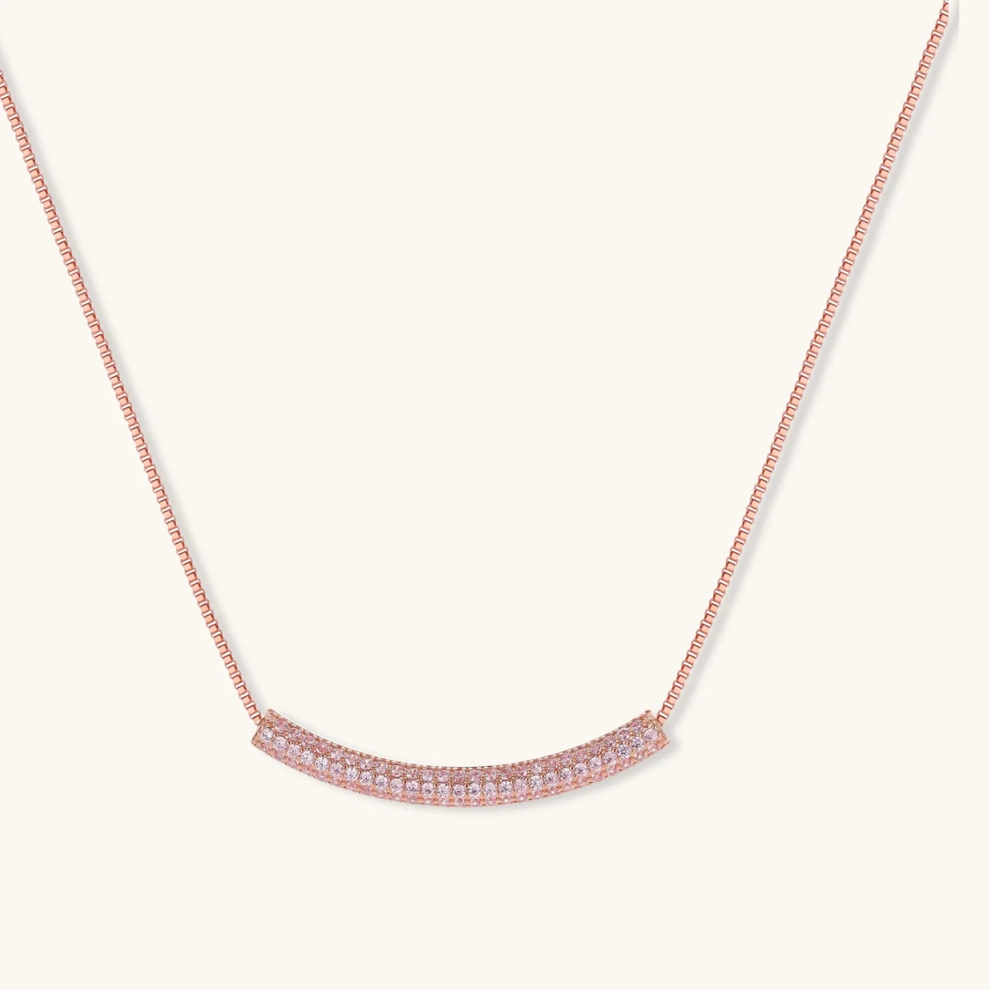 Rose gold jewelry set with pavé cubic zirconia stones including curved necklace, hoop earrings, and adjustable ring on cream background.